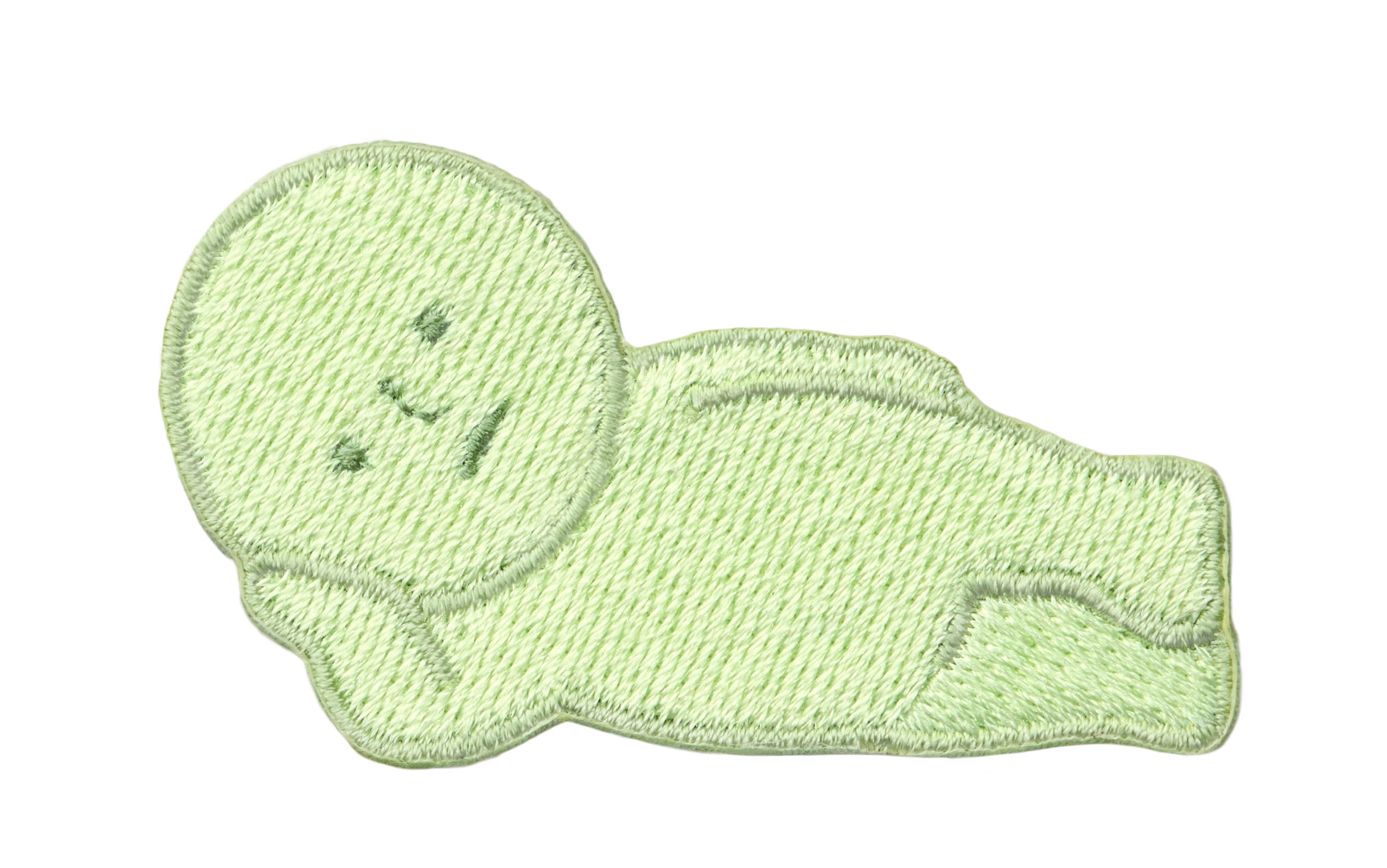 Image with transparent background shows SMISKI Embroidery Sticker "Lounging" SMISKI is a light green figure with dark green eyes, nose and mouth lying on their side, propped up by one hand. 