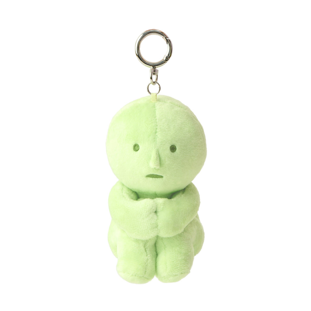 Image shows green plush SMISKI figure  with embroidery eyes and mouth is in a sitting position holding its knees. A silver loop and keychain clip is attached to its head. 