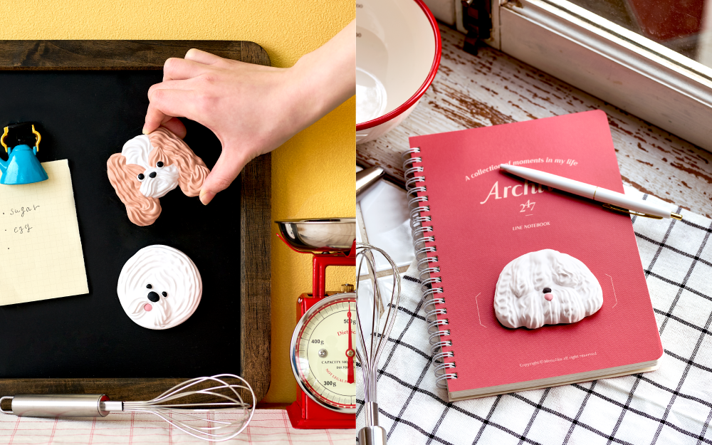 Split image; right side shows a hand placing the tan and white long eared dog Patissticker on a magnet board above a round white fluffy dog sticker. Right side: atop a red notebook, a fluffy white dog Patissticker is prominently shown on a tablecloth