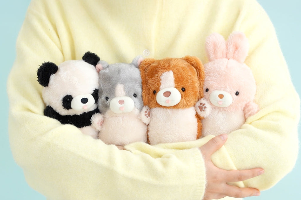 mugyuuus lifestyle image of person in yellow sweater holding pretzel (panda), peanuts (cat), waffle (beagle), and madeleine (bunny) left to right. 