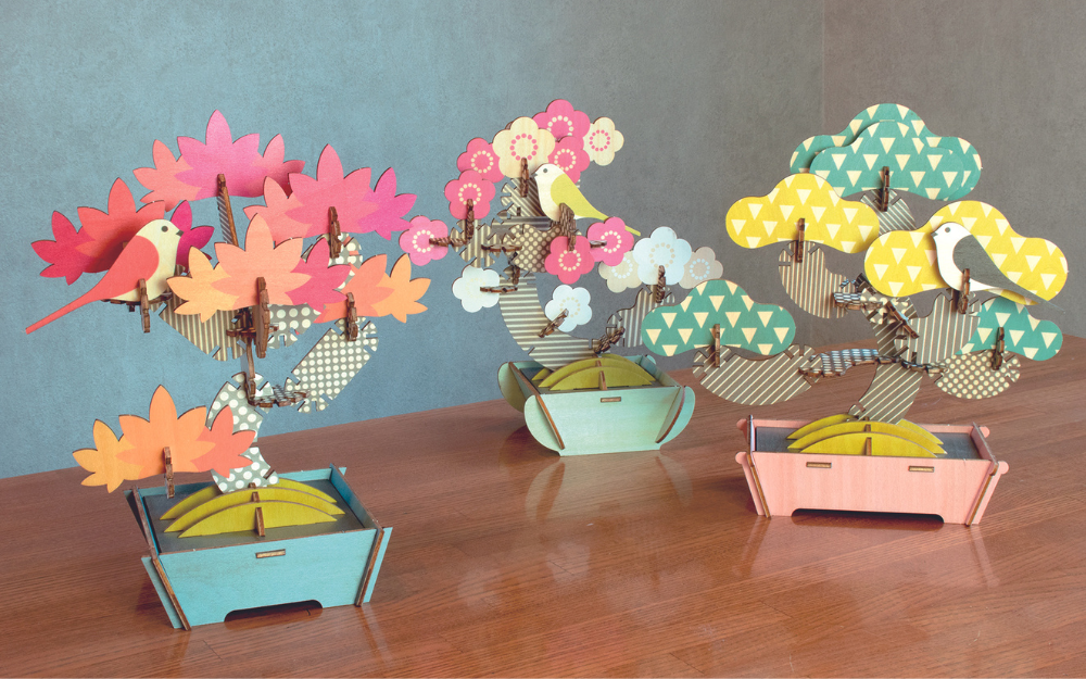 assembled displays of bonsai puzzle maple, apricot, and pine (left to right) on a table 
