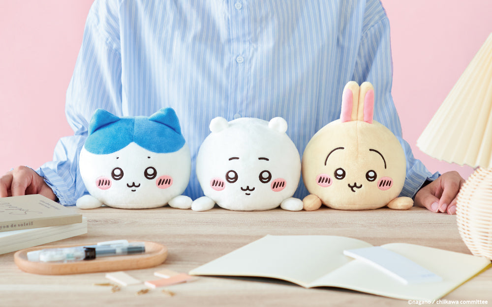 lifestyle banner image of posture pal chiikawa. front facing view of person in a blue striped shirt sitting at a desk with (left to right) hachiware, chiikawa, and usagi liked up at the desk in front of them.