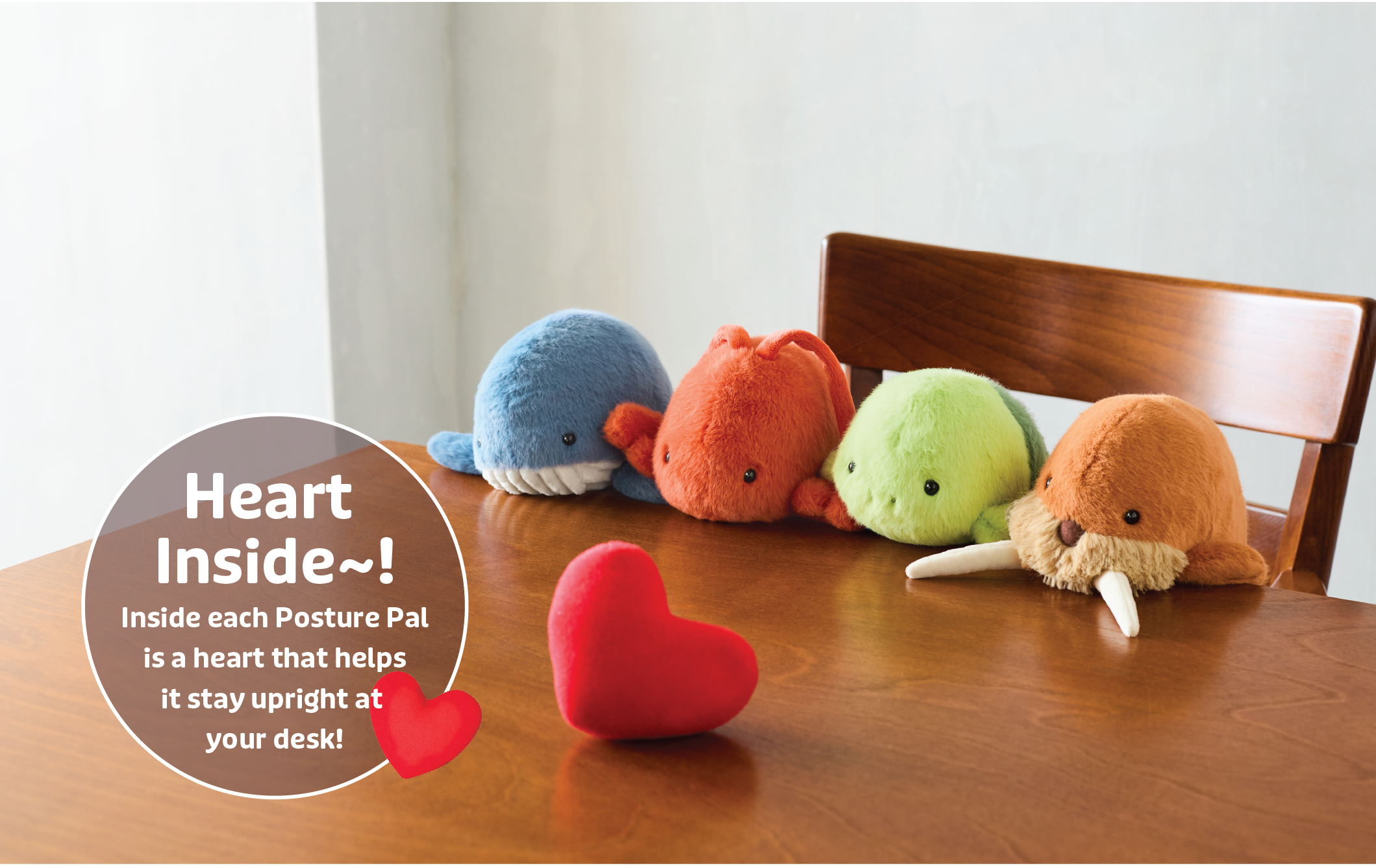 Image shows new lineup of Posture Pals- Marine. From left to right; blue whale, red/orange lobster, green turtle, brown walrus. Posture Pals sit on a wooden chair at a wooden table. A red heart also sits on the wooden table. Image include text: "Heart Inside~! Inside each Posture Pal is a heart that helps it stay upright at your desk!" text overlaid with a heart image. The images are set on a white background. 