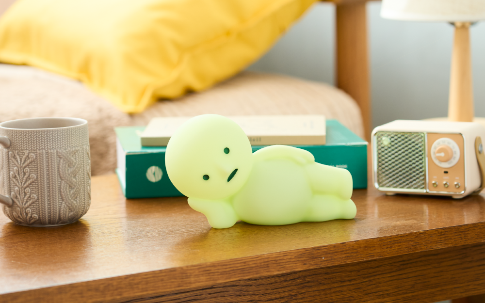 SMISKI Touch Light, Lounging, on a wooden surface with a mug, books, yellow pillow, and a radio in the background.