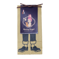 Image on transparent background shows "Maekake" apron as a poster image set atop an illustration of legs and feet. The apron design depicts Rabbit Sonny Angel beside Robby encircled with concentric circles and cherry blossoms, and text: "Sonny Angel" "He may bring you happiness?!". Rabbit Sonny Angel minifigure is shown in a small red and white pocket. 